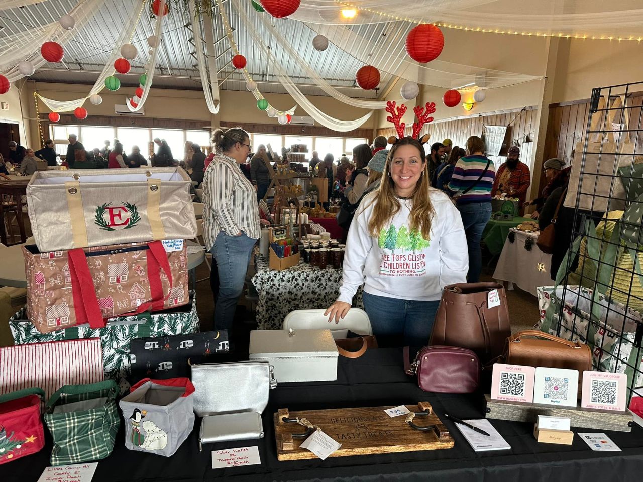 A woman tends a table at a holiday market indoors. 